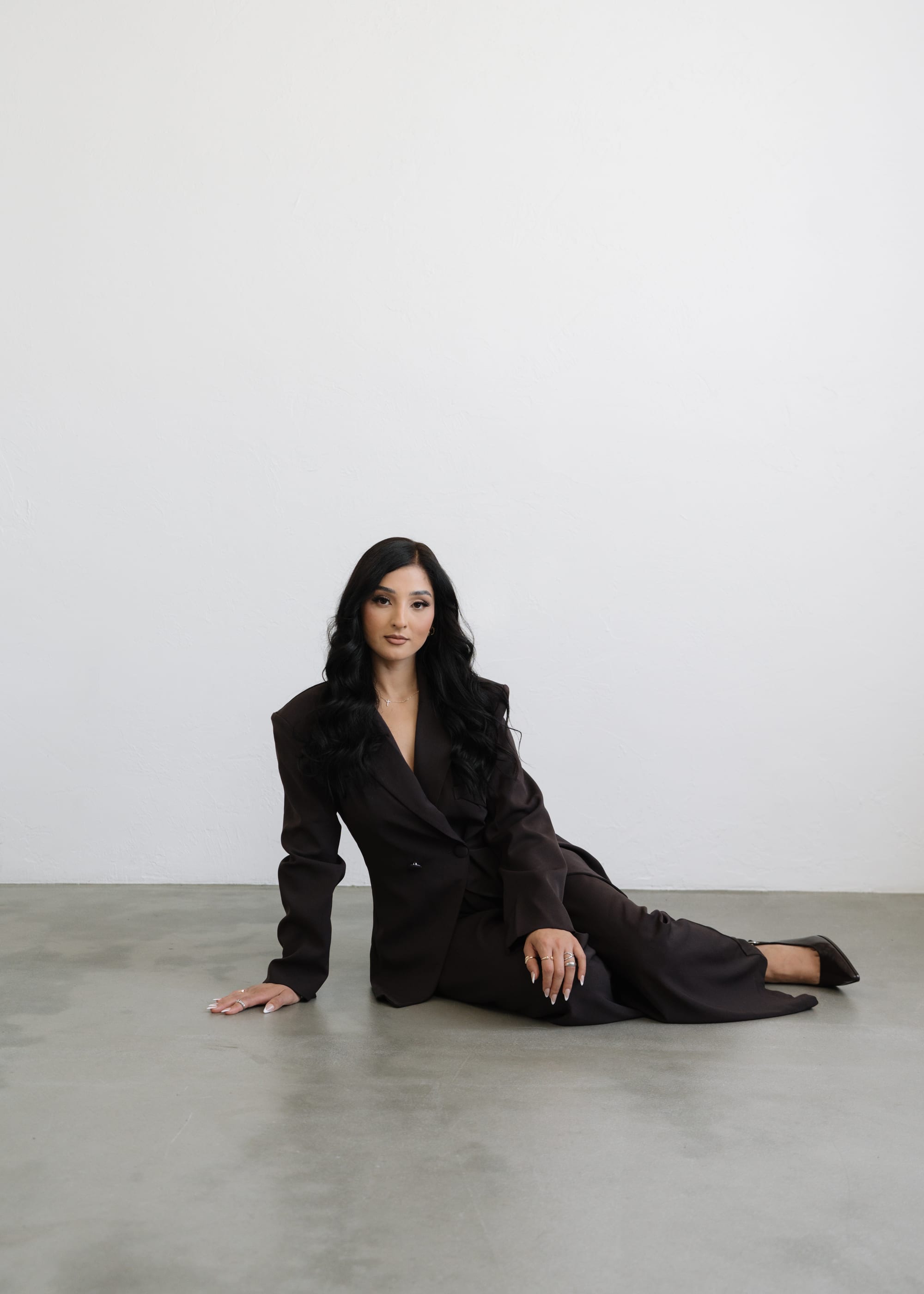 Elizabeth Valdovinos seated on the studio floor in a black suit
